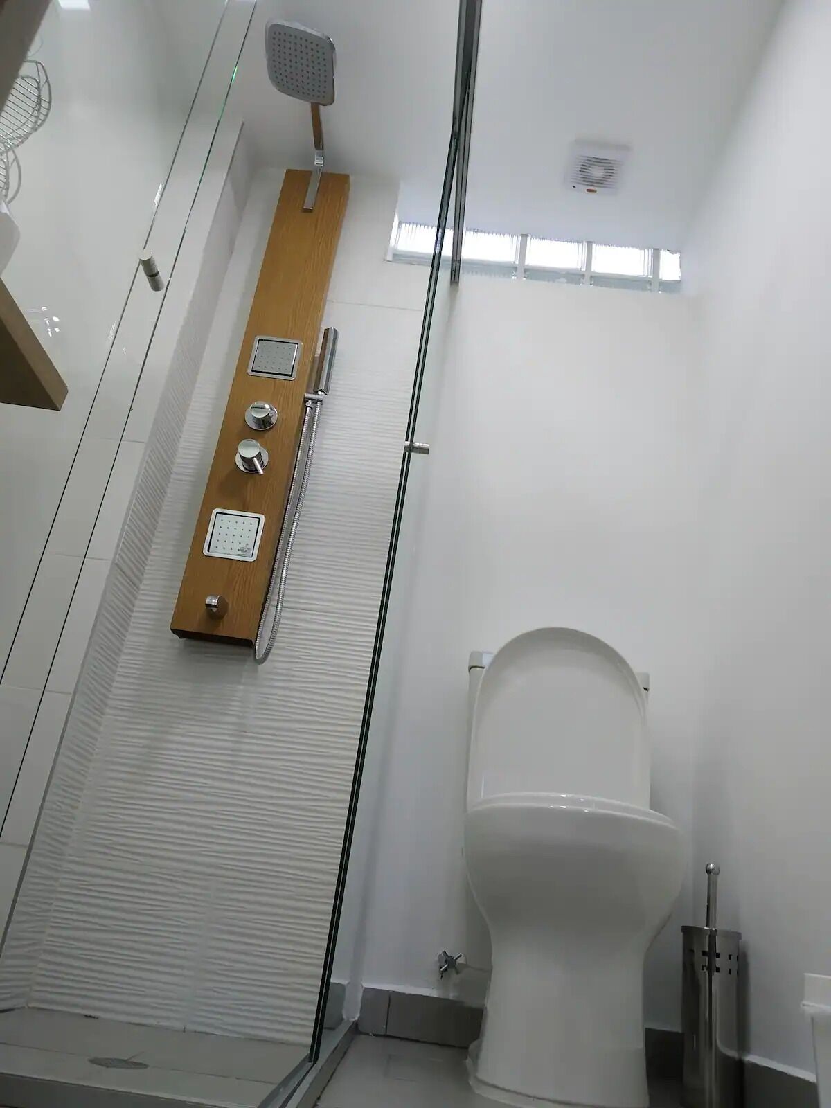 A modern bathroom with a shower, toilet, and a wooden panel with controls.