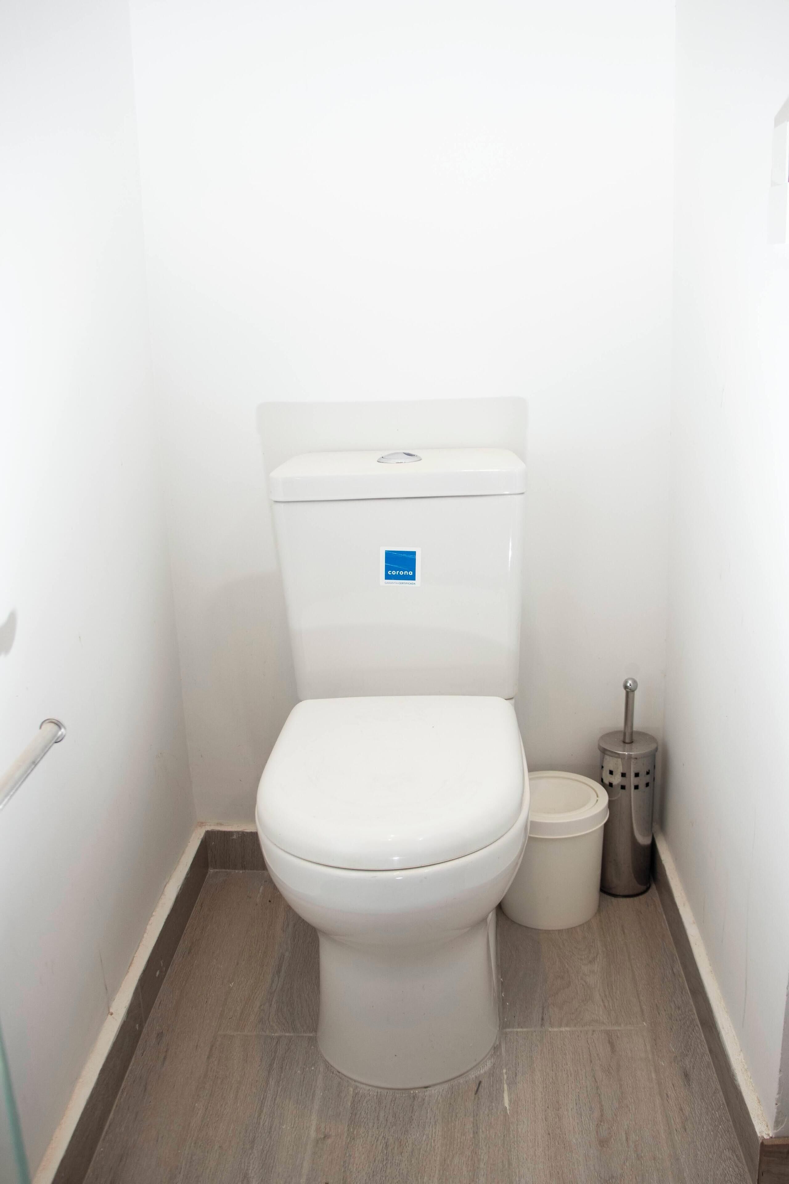 A small, clean bathroom with a white toilet, a trash bin, and a toilet brush.