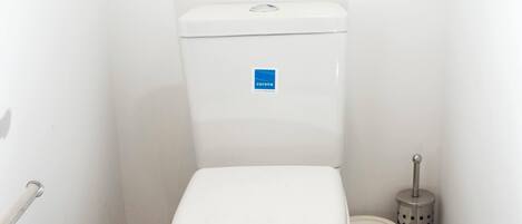 A small, clean bathroom with a white toilet, a trash bin, and a toilet brush.