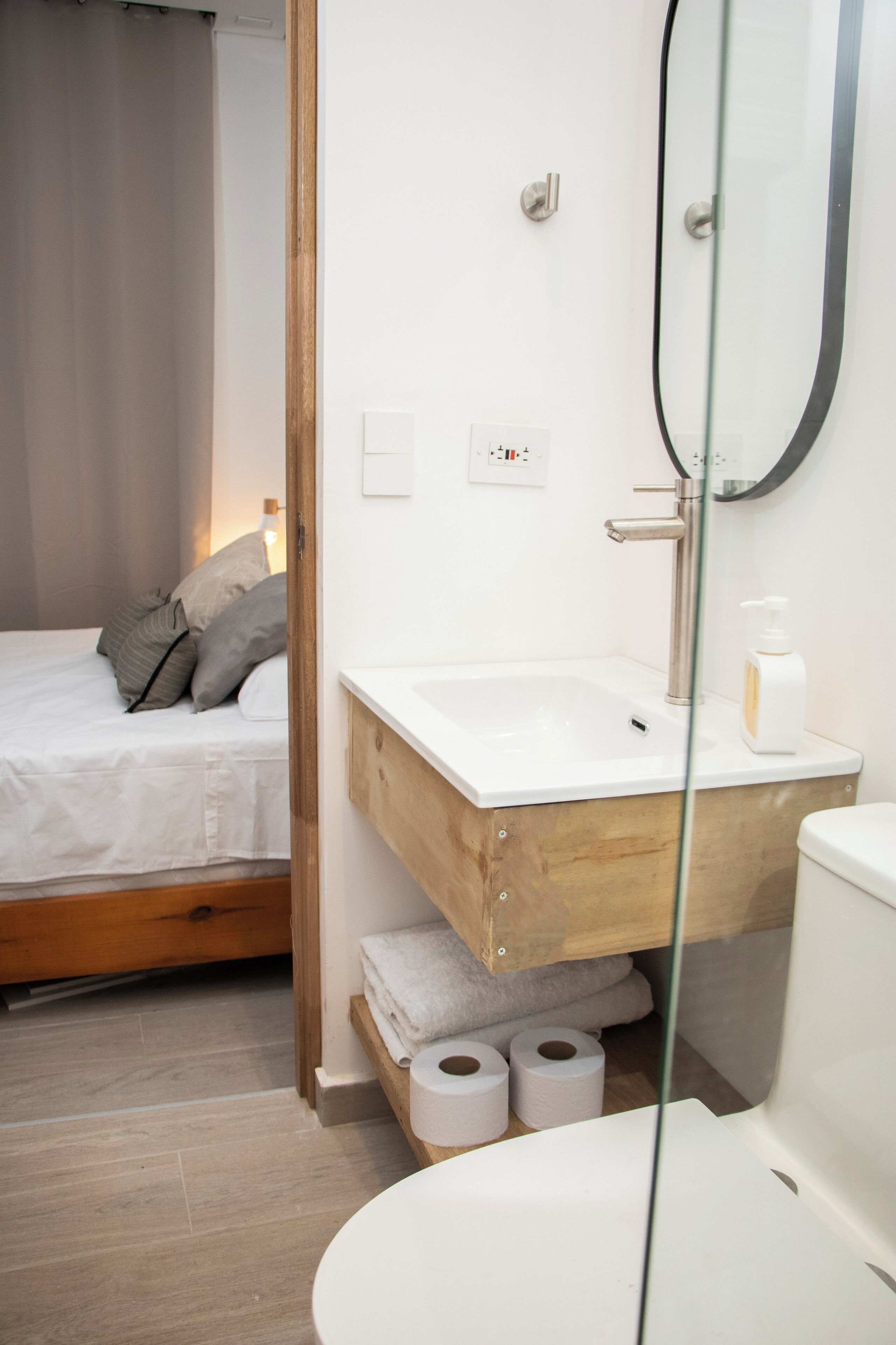 A modern bathroom with a wooden vanity, a glass shower enclosure, and a bed with a curtain.