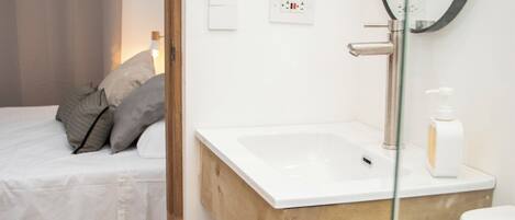 A modern bathroom with a wooden vanity, a glass shower enclosure, and a bed with a curtain.