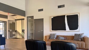 A modern living room with a large abstract painting, a brown sofa with patterned cushions, and two black upholstered chairs. - Thomas Rd Oasis (Scottsdale)