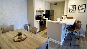 A modern kitchen with white cabinets, stainless steel appliances, and a central island with bar stools. - Thomas Rd Oasis (Scottsdale)