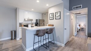 A modern kitchen with white cabinets, a stainless steel refrigerator, and a bar area with stools. - Thomas Rd Oasis (Scottsdale)