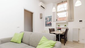 A modern living room with a grey sofa and green cushions, a dining area with a table and chairs, and a kitchen visible in the background. - VivimiHome-Duomo Cioffi House (Milan)