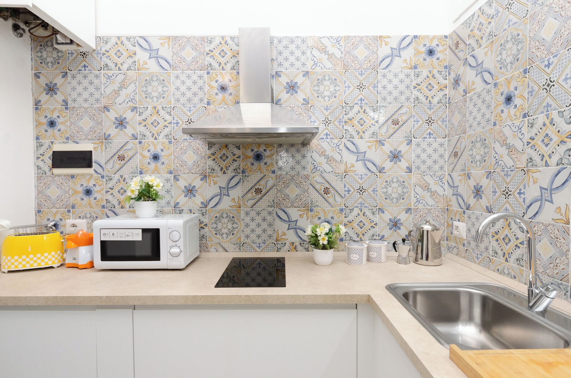 A kitchen with a microwave, toaster, and sink. There are decorative tiles on the wall and a potted plant on the counter.
