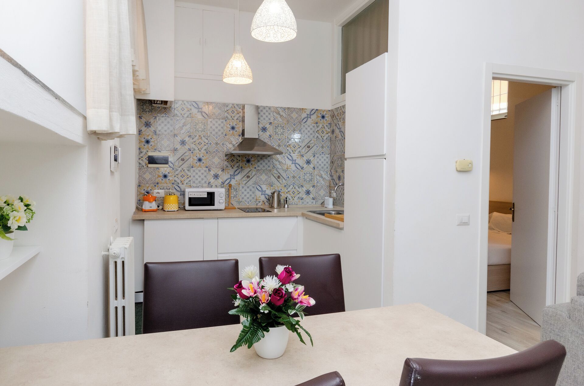 A modern kitchen with white cabinets, a tiled backsplash, and a dining area with a table and chairs.