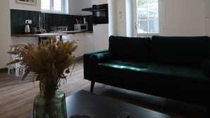A modern living room with a dark green sofa, a coffee table with a vase and candle, and a kitchen in the background.