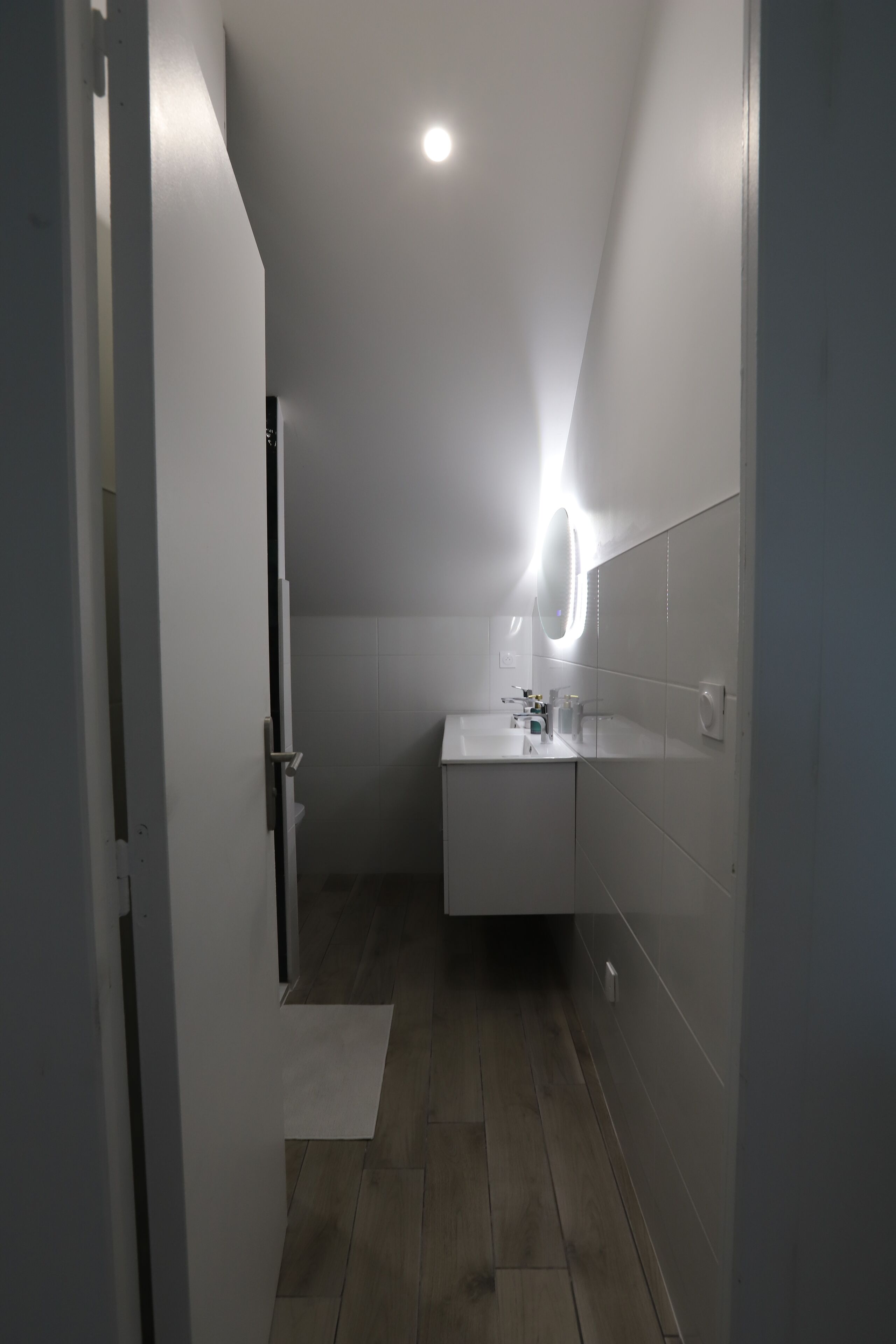 Un corridoio stretto che porta a un bagno con lavandino bianco, specchio e pareti piastrellate.