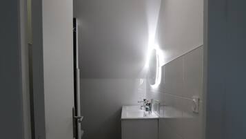 Un corridoio stretto che porta a un bagno con lavandino bianco, specchio e pareti piastrellate.