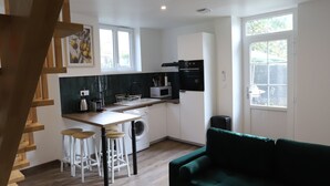 A modern apartment with a kitchen, dining area, and living room. It includes a staircase, a green sofa, and a vase with dried flowers.