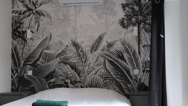 A bedroom with a large bed, a wall-mounted air conditioner, and a tropical leaf-patterned wallpaper.