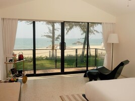 A hotel room with a large sliding glass door leading to a balcony with a view of the beach and ocean.