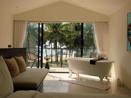 A modern bathroom with a freestanding bathtub, a glass-enclosed shower area, and a view of the beach.