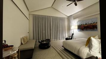 A hotel room with a bed, a sofa, a coffee table, a ceiling fan, and a painting on the wall.