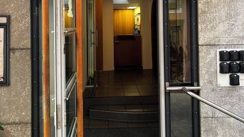 A reception area with a glass door, a sign above the door, a staircase leading inside, and a small outdoor planter with flowers.