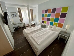 A hotel room with a large bed, a desk, a chair, a colorful wall art, and a small bedside table. - Altstadt Hotel Wertheim (Wertheim)