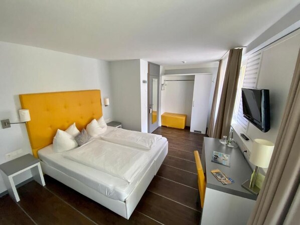 A hotel room with a double bed, a bedside table, a TV, and a small desk with a lamp. - Altstadt Hotel Wertheim (Wertheim)