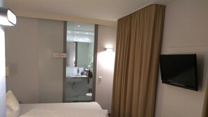 A hotel room with a bed, a television, a bathroom visible through a glass partition, and a curtain. - Altstadt Hotel Wertheim (Wertheim)