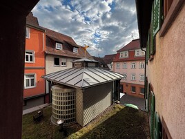 Un patio con estructura de techo metálico, un depósito de agua cilíndrico y edificios adyacentes con fachadas rojas y rosadas.