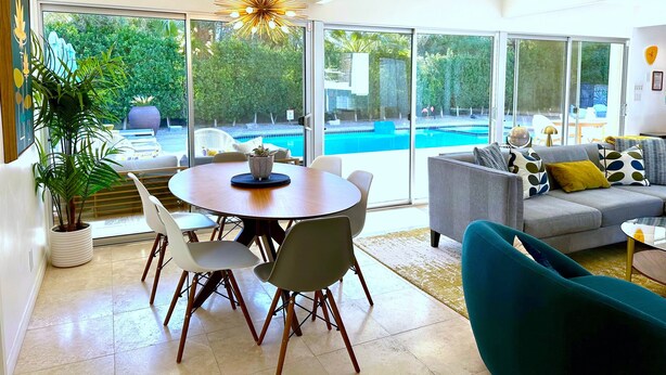 Un salon moderne avec vue sur la piscine, un coin repas et un canapé agrémenté de coussins à motifs.