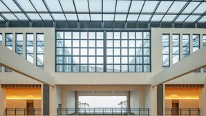 Un atrio de varios niveles con techo de vidrio, ventanas amplias y un espacio abierto central con vistas al exterior.