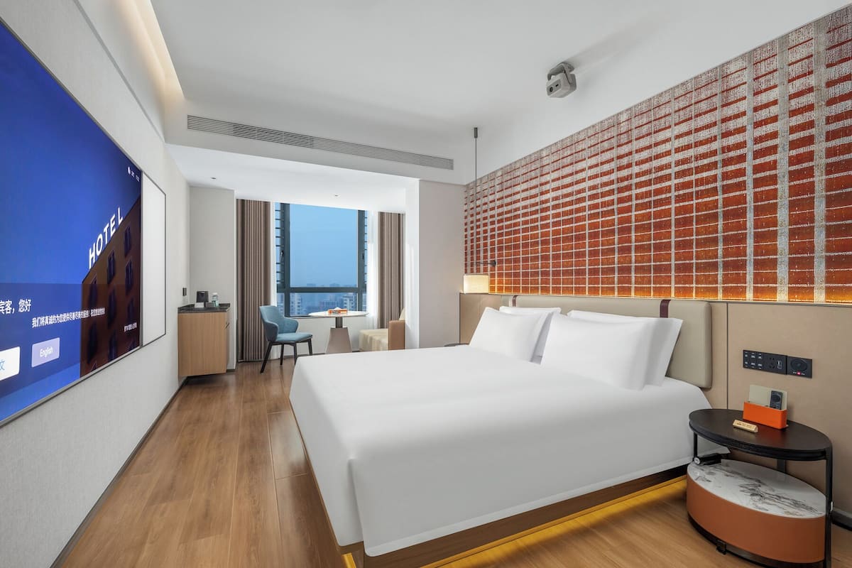 Une chambre d’hôtel avec un grand lit, un bureau, une chaise, une petite table et un téléviseur fixé au mur.