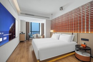 Habitación de hotel con una cama grande, un escritorio, una silla, una mesita y un televisor en la pared.