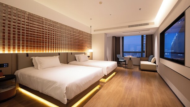 Una habitación de hotel moderna con dos camas, una zona de estar y un ventanal con vistas a la ciudad.