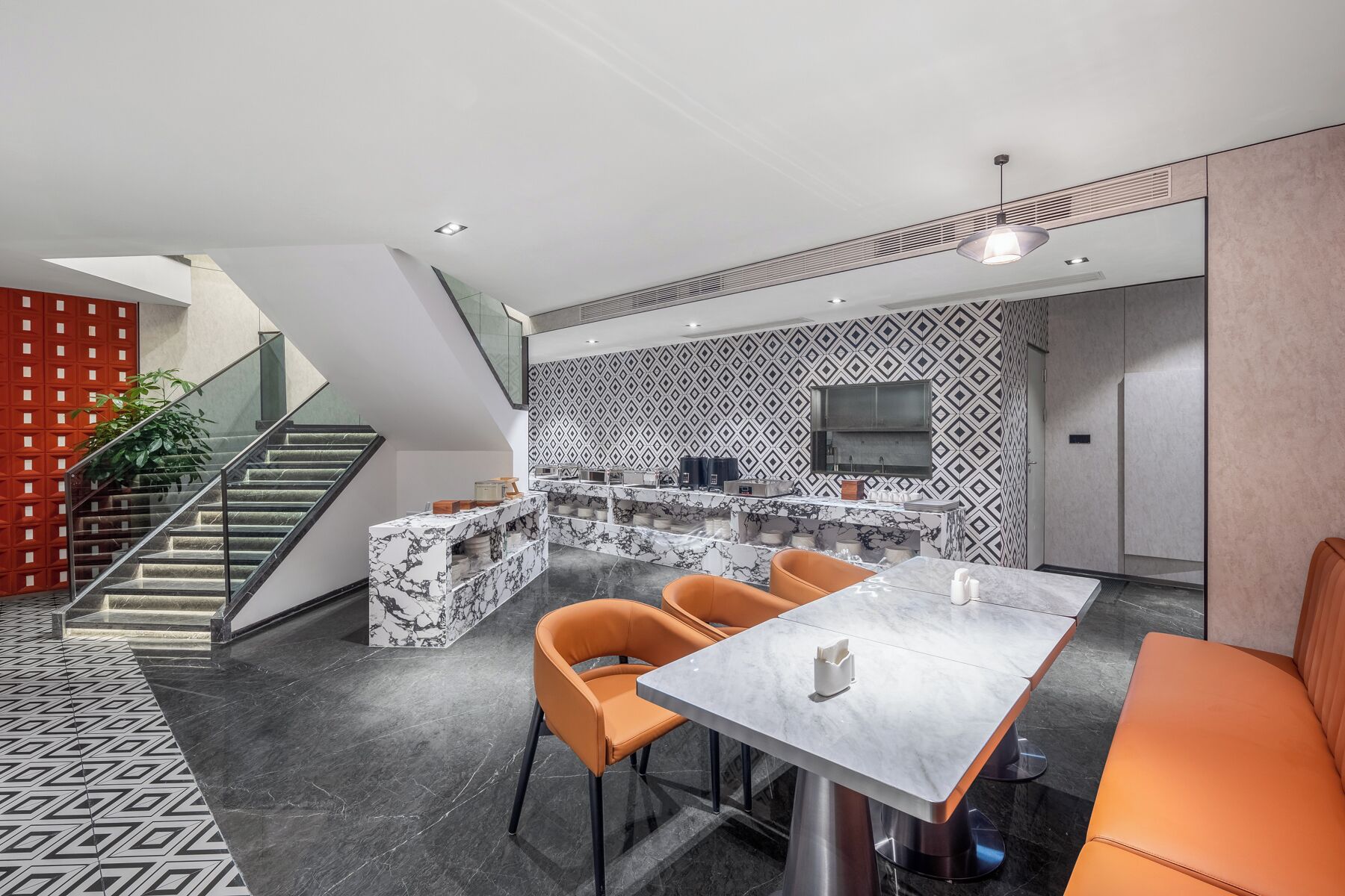 Una cocina moderna con una isla de mármol, un comedor con mesa y sillas, y una escalera con una pared de acento roja.