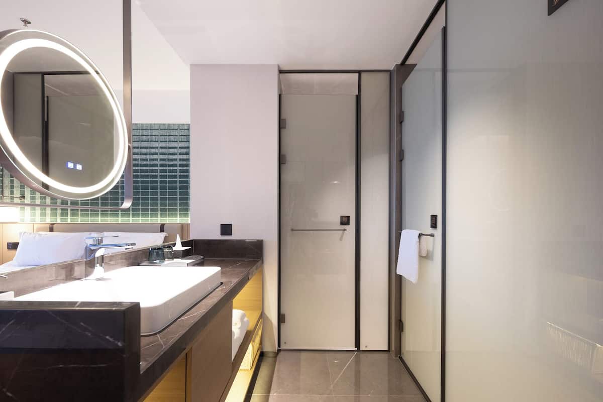 Une salle de bain moderne avec un grand miroir, deux lavabos et une porte en verre donnant sur l’espace de la douche.