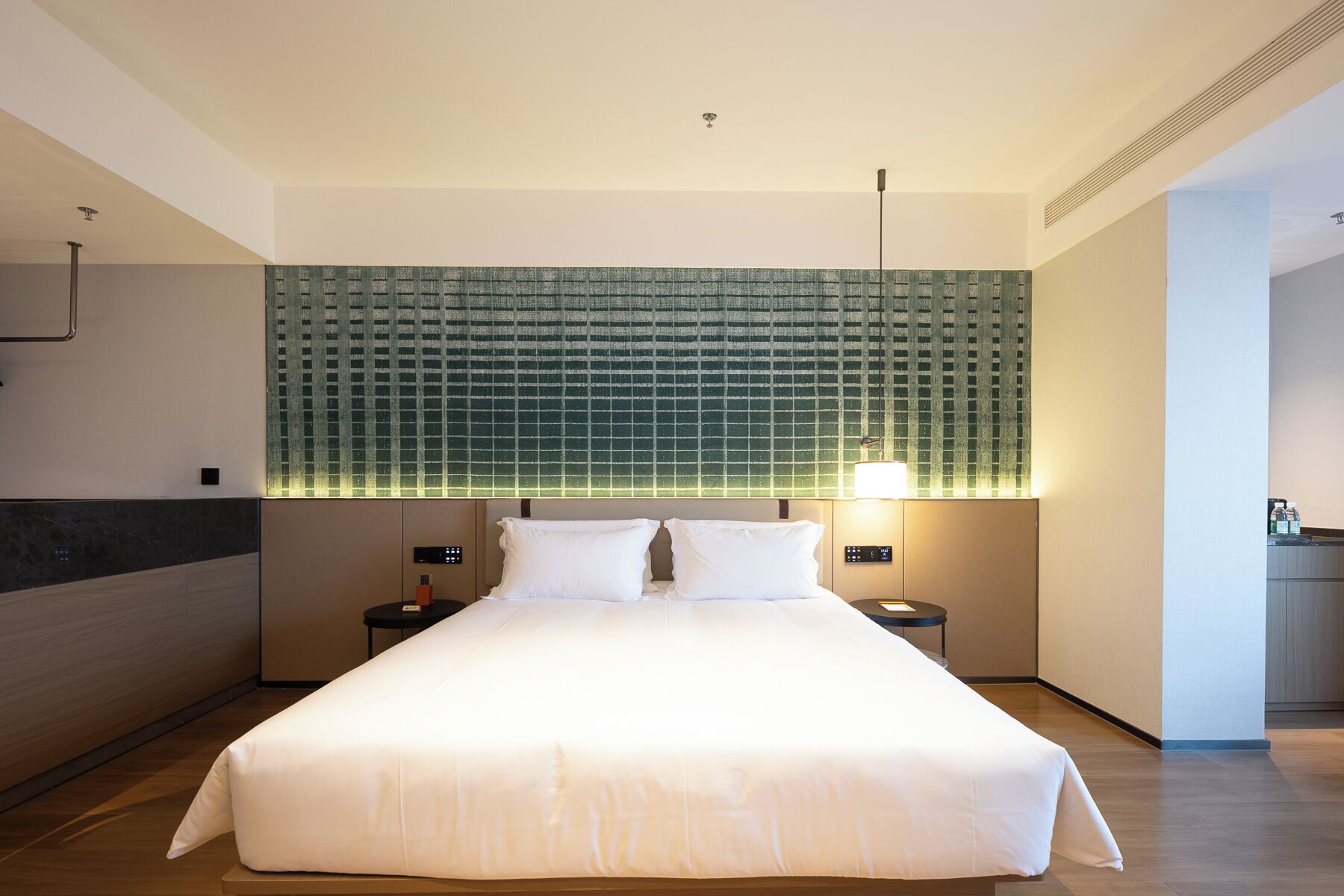 Una habitación de hotel moderna con una cama grande, dos mesitas de noche, un panel de control en la pared y un cabecero verde con estampado.