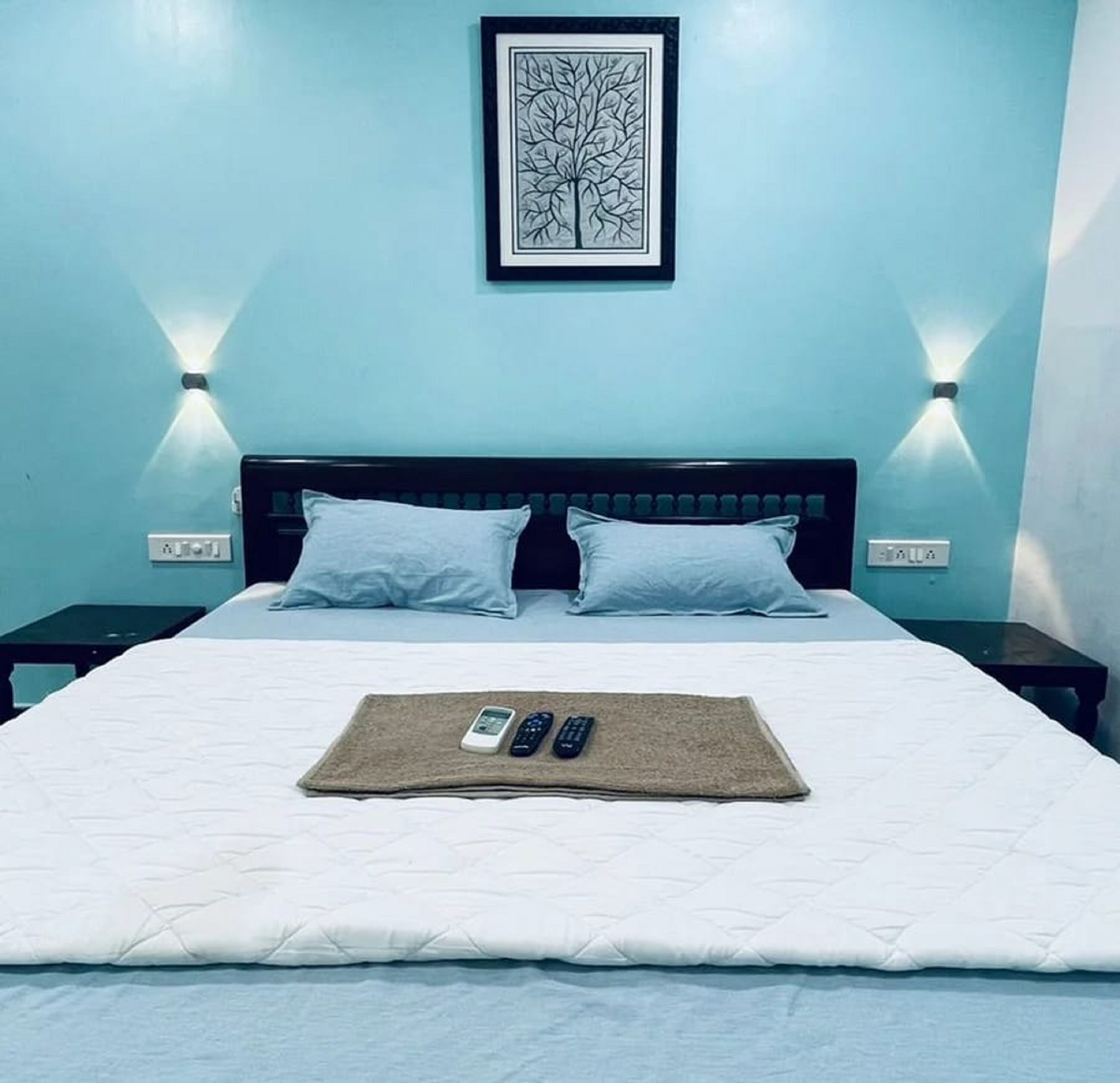 A neatly made bed with a white duvet, two pillows, and a remote control set on a beige throw.