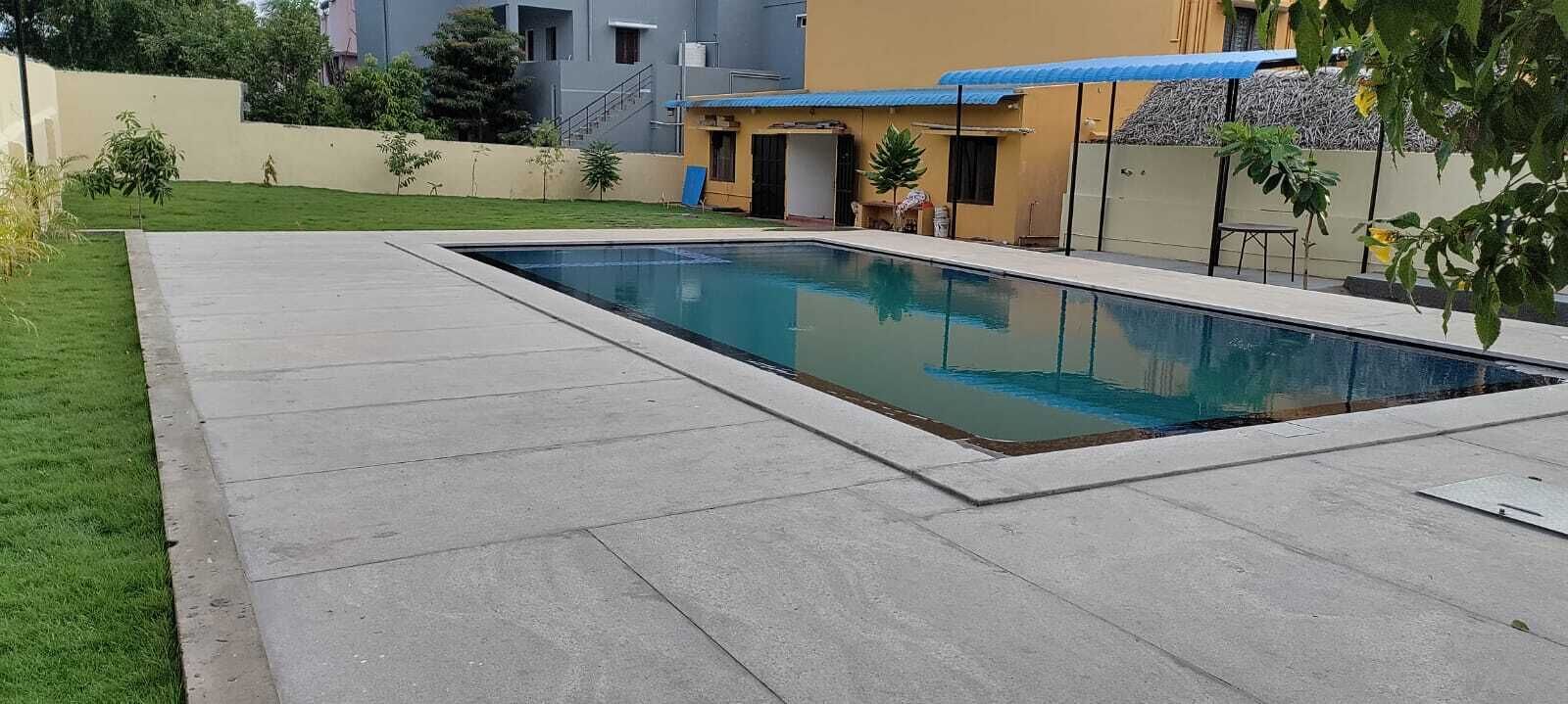 A rectangular swimming pool with a concrete deck, surrounded by a well-maintained lawn and a few small trees.