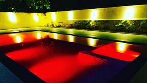 A rectangular pool with a red hue, surrounded by a low wall and illuminated by overhead lights. - VCP Beach Resort (Puducherry)