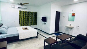 A room with a bed, a sofa, a small table, a TV, and a ceiling fan. - VCP Beach Resort (Puducherry)