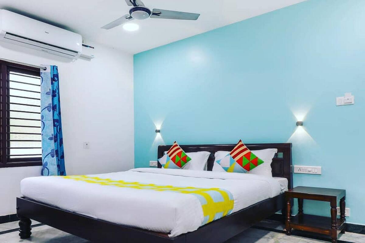 Un dormitorio con cama, ventilador de techo, ventana con cortinas y mesita de noche.