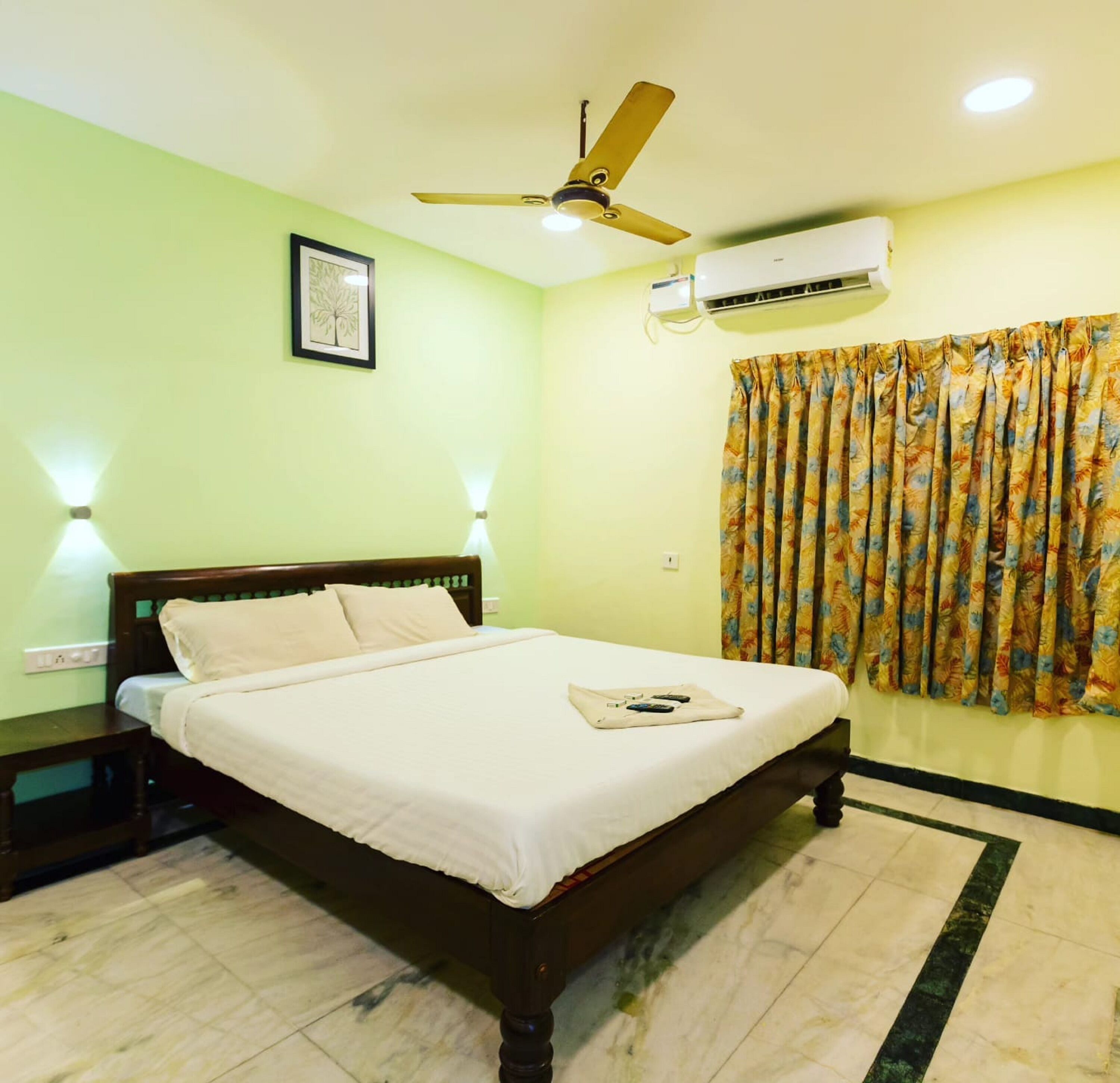 A bedroom with a bed, a ceiling fan, an air conditioning unit, and a floral curtain.