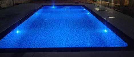 A rectangular pool with a blue-lit surface, surrounded by a stone deck.