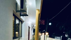 A narrow outdoor corridor with potted plants on either side, a central pillar, and a building entrance with an air conditioning unit. - VCP Beach Resort (Puducherry)
