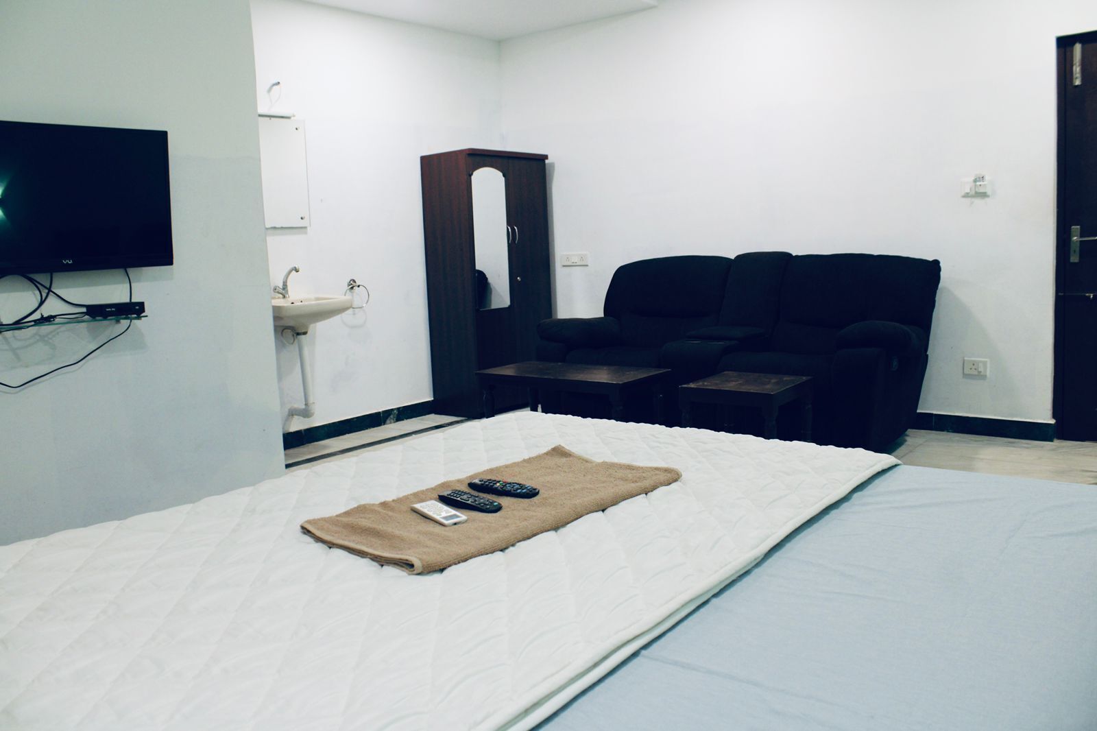 Habitació d'hotel amb un llit, una televisió penjada a la paret, un rentapla, un mirall, dues cadires i una taula petita.