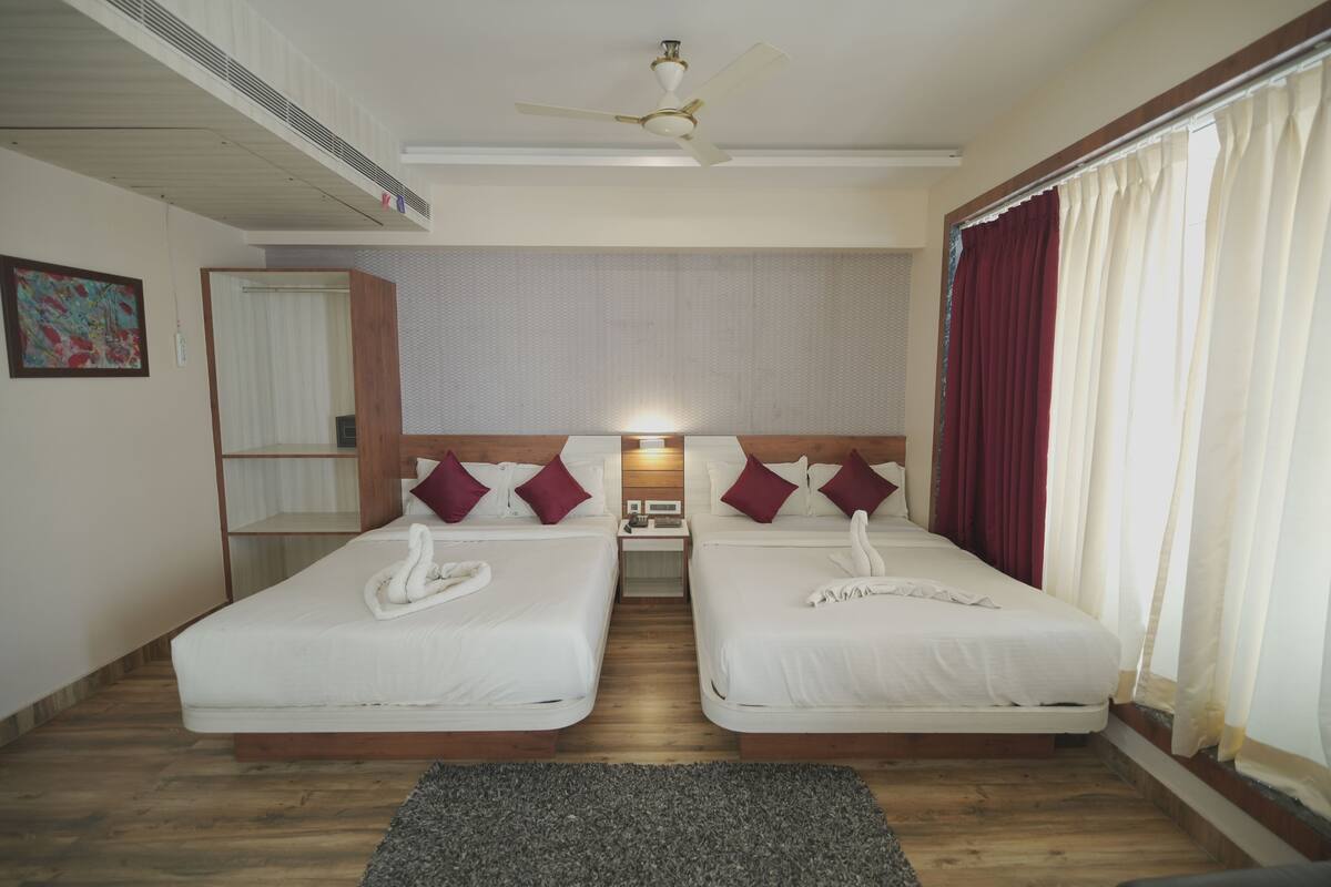 Habitación de hotel con dos camas, un ventilador de techo, una mesita de noche y una ventana con cortinas.