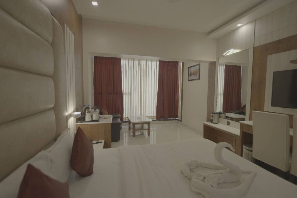 Habitación de hotel con una cama grande, un escritorio, una silla, un televisor y una ventana con cortinas.