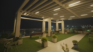Una terrazza esterna con posti a sedere, fioriere e vista sulla città di notte.