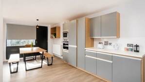 A modern kitchen with grey cabinets, a wooden countertop, and a dining area with a table and bench. - Student Only Zinc Quarter (Bristol)