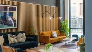 A modern living room with a dark blue sofa, a mustard-colored sofa, and a green armchair. There are two black wall-mounted lamps, a large potted plant, and a framed picture on the wall. - Student Only Zinc Quarter (Bristol)