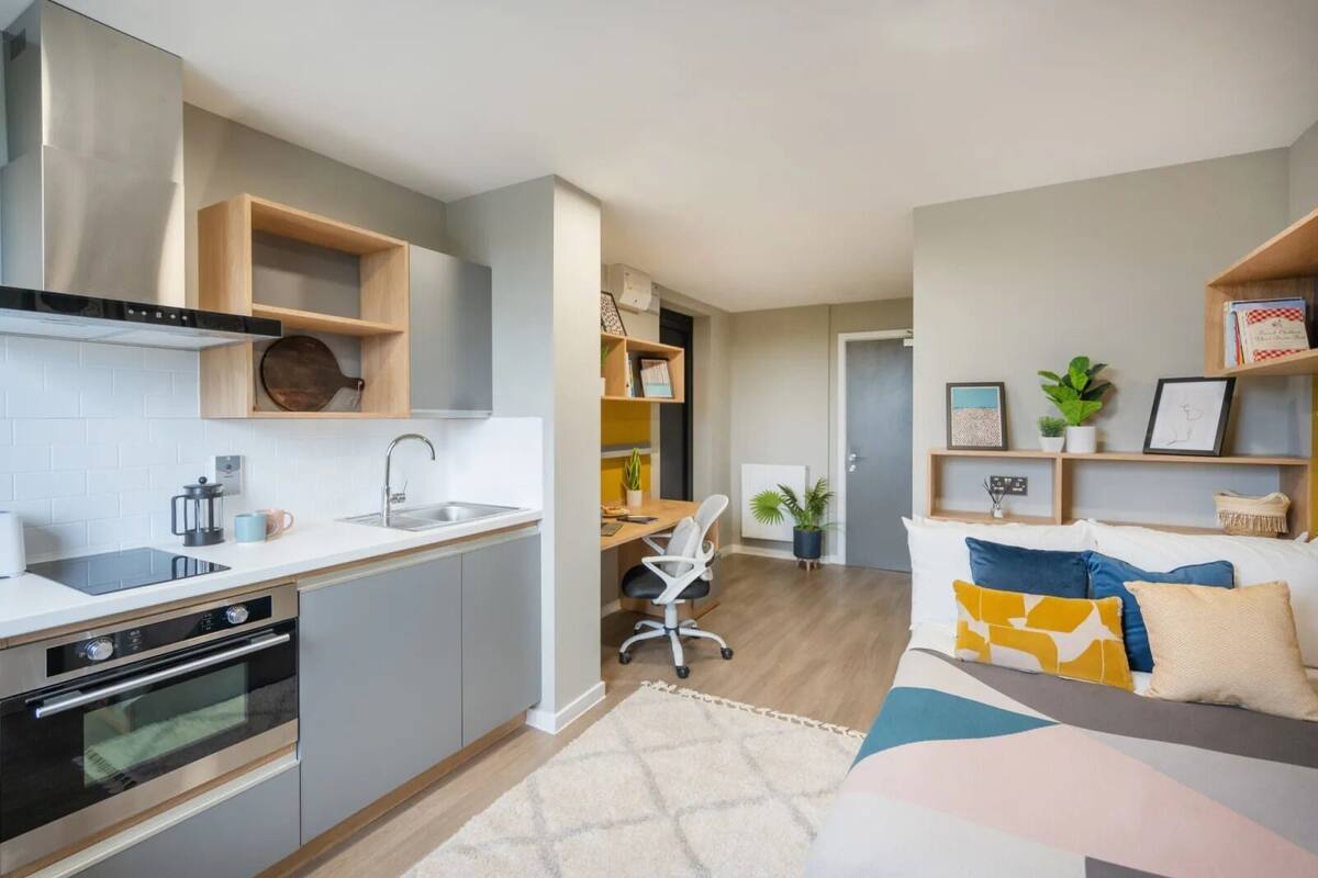 A modern kitchen with built-in appliances, a dining area with a table and chairs, and a living room with a sofa and decorative pillows.