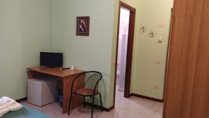 Una habitación pequeña con escritorio, silla y televisor. Hay una puerta que da a otra habitación.