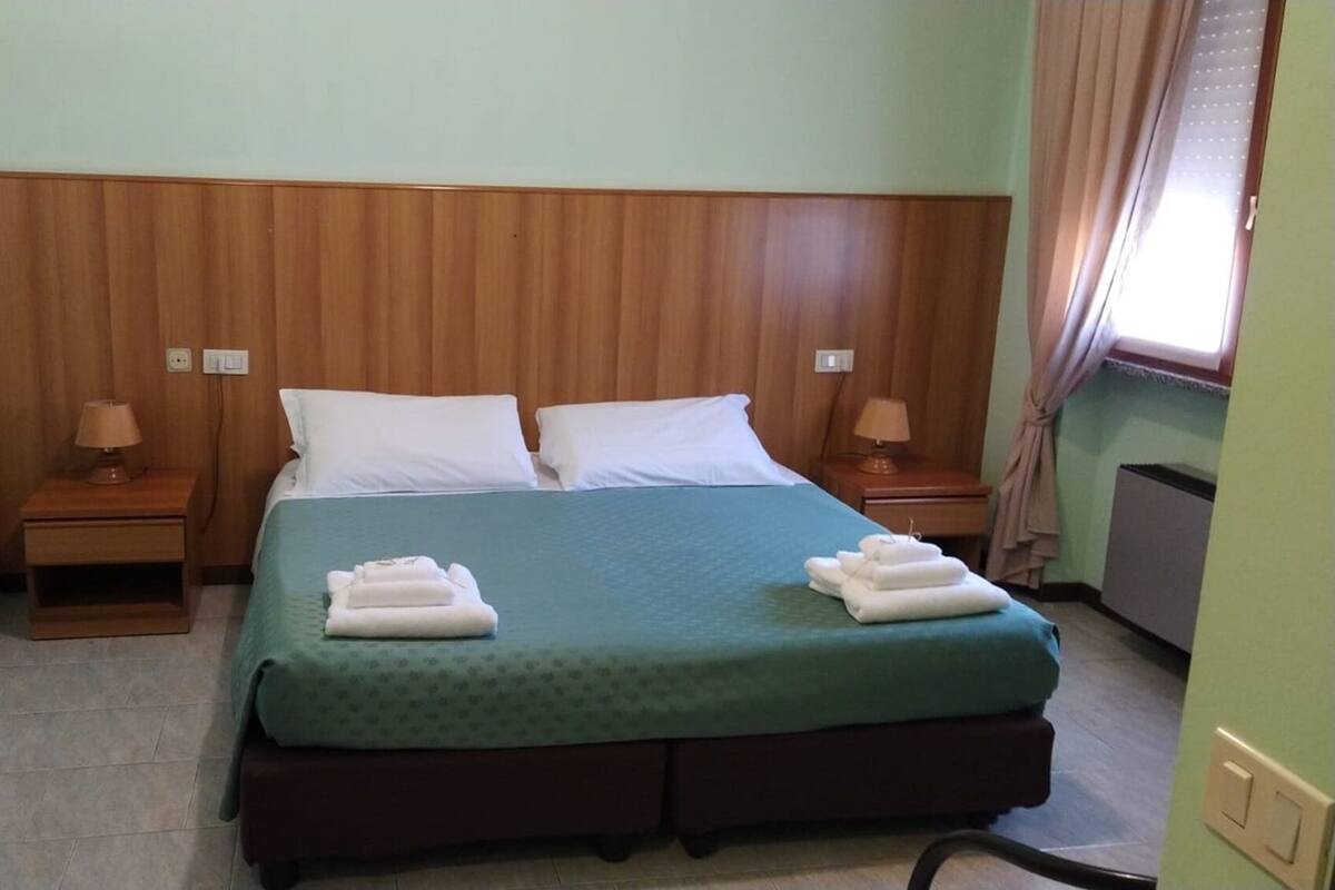 A hotel room with a wooden headboard, two beds with white linens, two bedside tables with lamps, and a green bedspread.