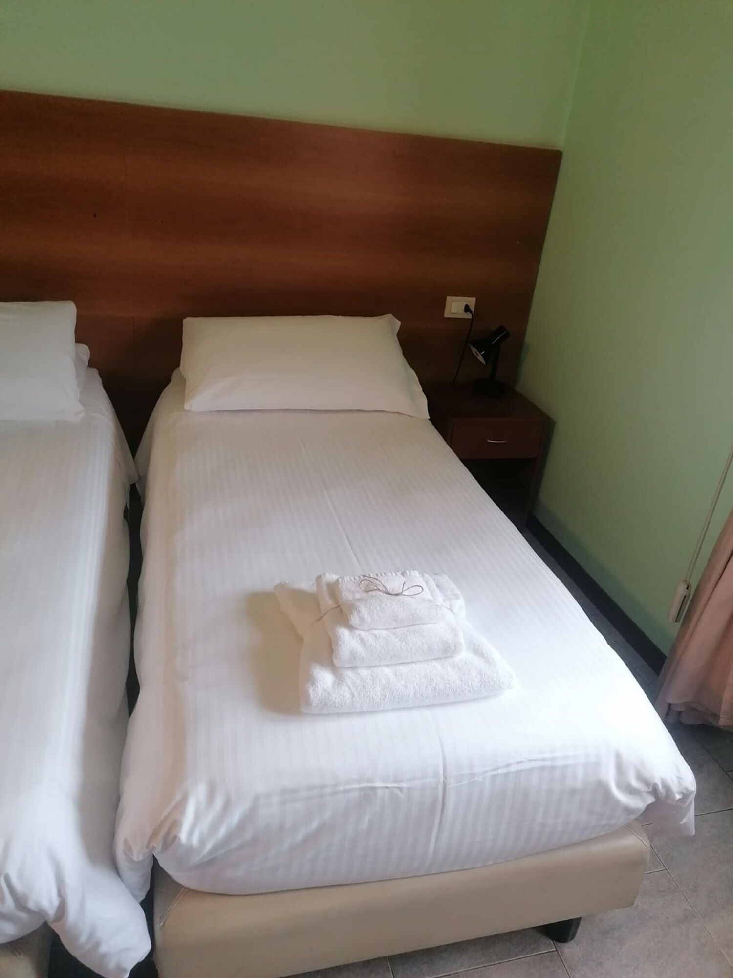 Ein Hotelzimmer mit zwei Betten, jeweils mit weißen Leinen und Kissen, einem Holz-Kopfteil, einem Nachttisch mit Lampe und einem gefalteten Handtuch auf dem Bett.